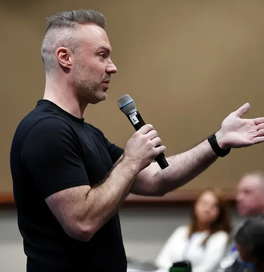 Rick Jordan speaking to a small room with a microphone in hand